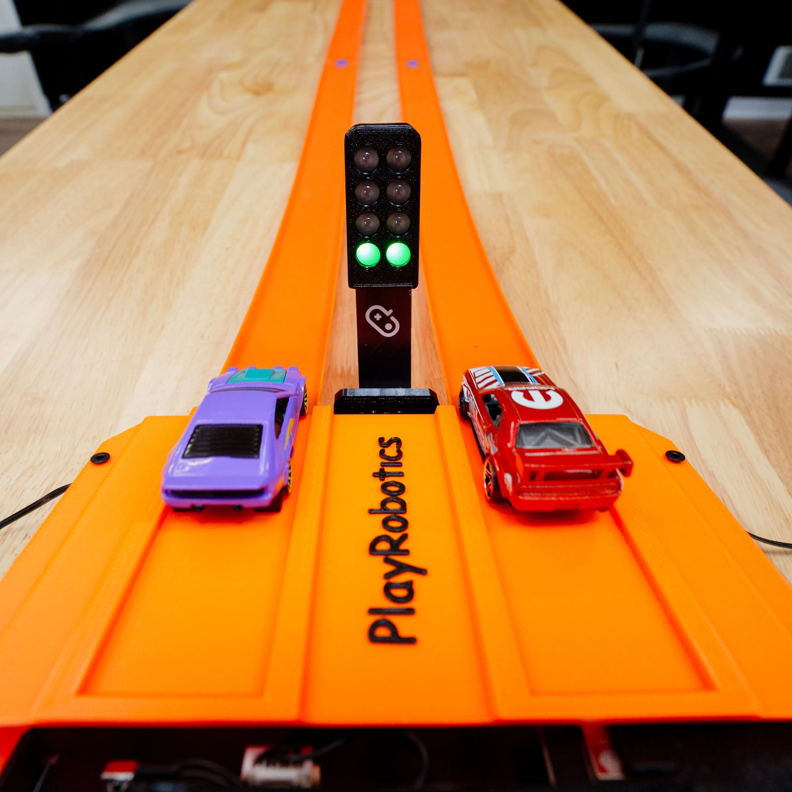 HotWheels cars on an orange track with a control panel, on a table.
